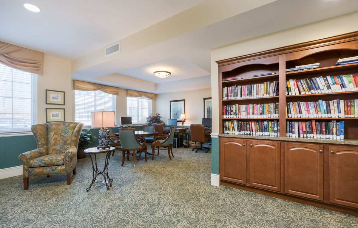 A cozy library room with bookshelves, seating, and large windows.