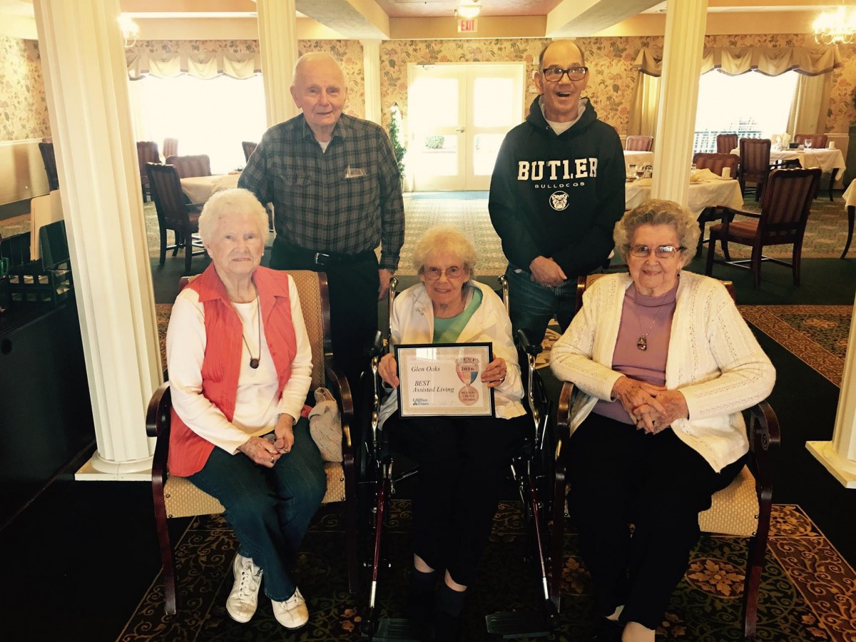 A group of seniors gathering for a family photo indoors, with one person holding an award.
