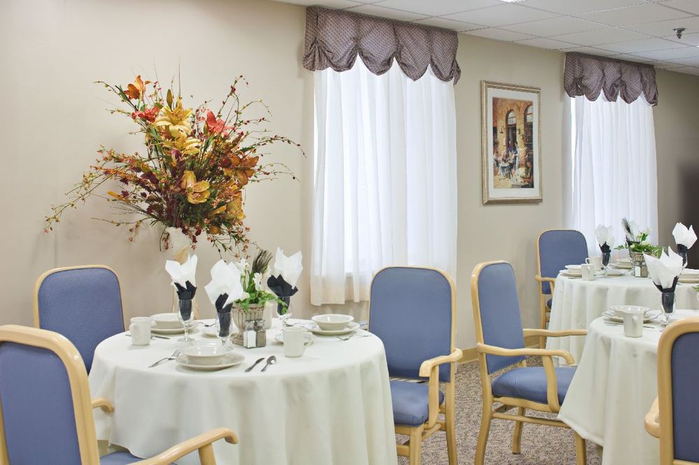 A well-decorated dining room with neatly arranged tables and chairs, featuring floral centerpieces and elegant curtains.