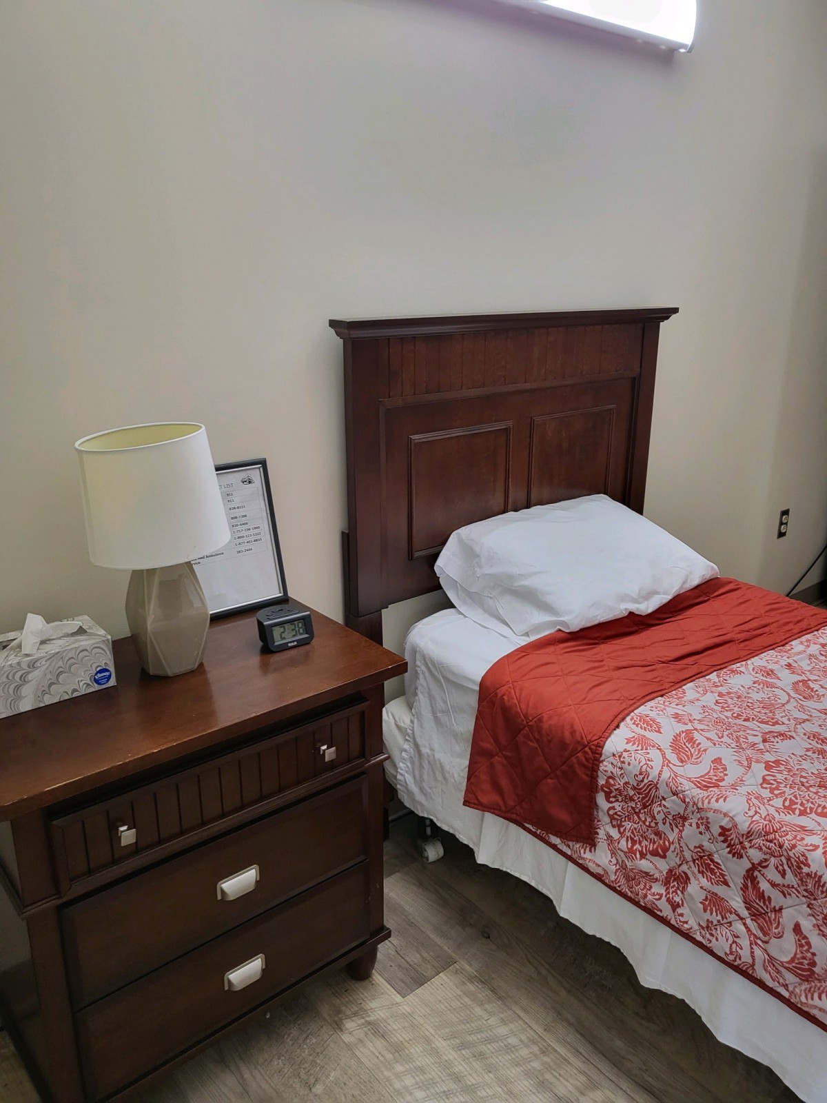 A neatly arranged single bed with a wooden headboard, accompanied by a nightstand and lamp in a simple bedroom setting.