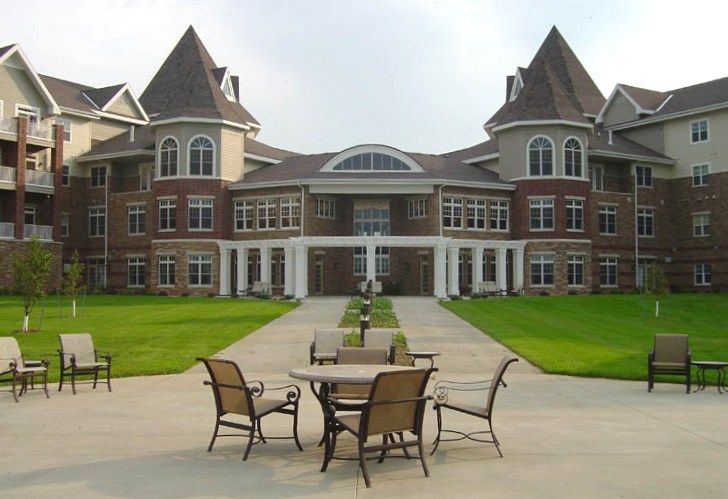 A large, elegant building with a central courtyard featuring outdoor seating and well-maintained lawns.