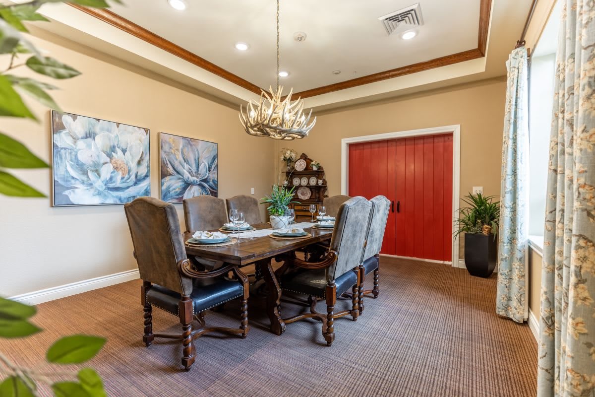 A cozy dining room with a wooden table, upholstered chairs, and a unique chandelier, adorned with artwork and decorative plants.