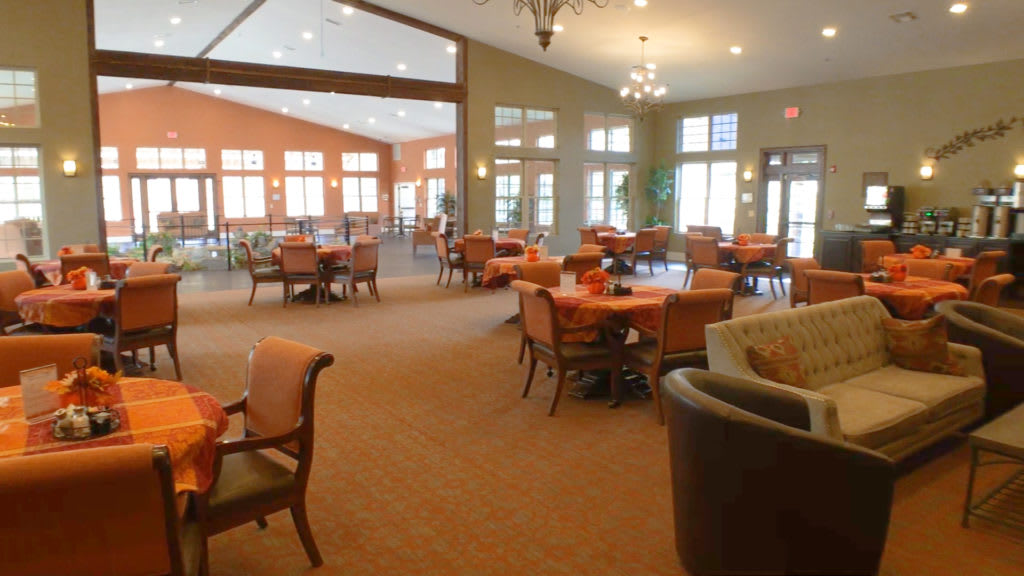 A spacious dining room with arranged tables and chairs, well-lit by natural light through large windows.