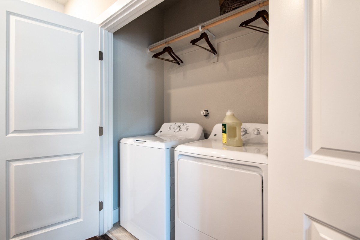 A compact laundry area featuring a washing machine, dryer, and shelves with hangers.
