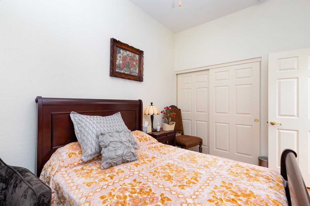 A cozy bedroom with a floral bedspread, decorative pillows, a lamp on the nightstand, and a painting above the bed.
