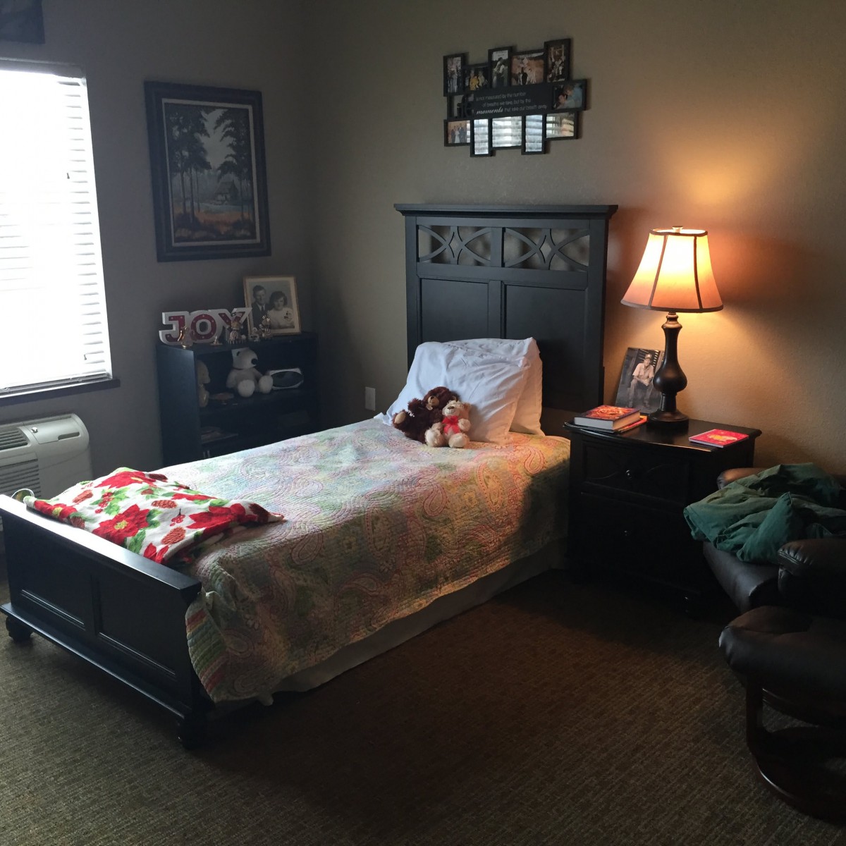 A cozy bedroom with a single bed, nightstand, and a lit lamp by the window.