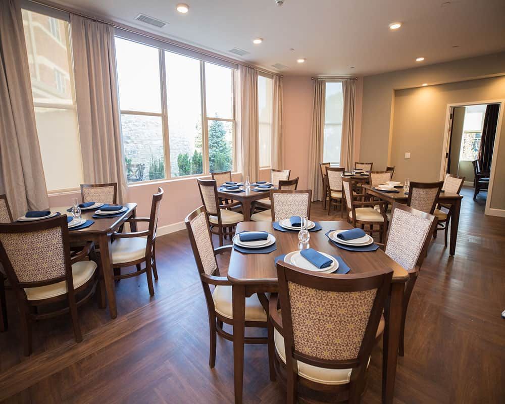 A modern dining room with neatly arranged tables and chairs, filled with natural light.