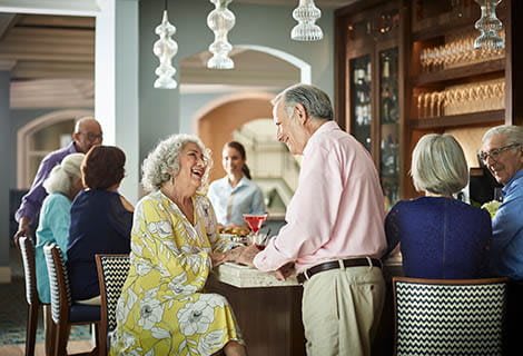 Two senior individuals enjoy a conversation at a bar in a restaurant setting.