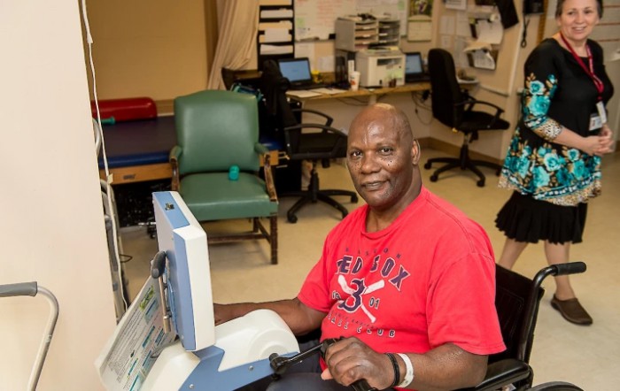 A man smiling while sitting at a desk with a computer in an office setting.