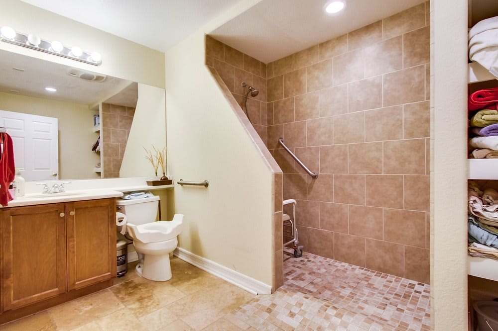 An accessible bathroom with a walk-in shower, equipped with grab bars and a wooden stool.