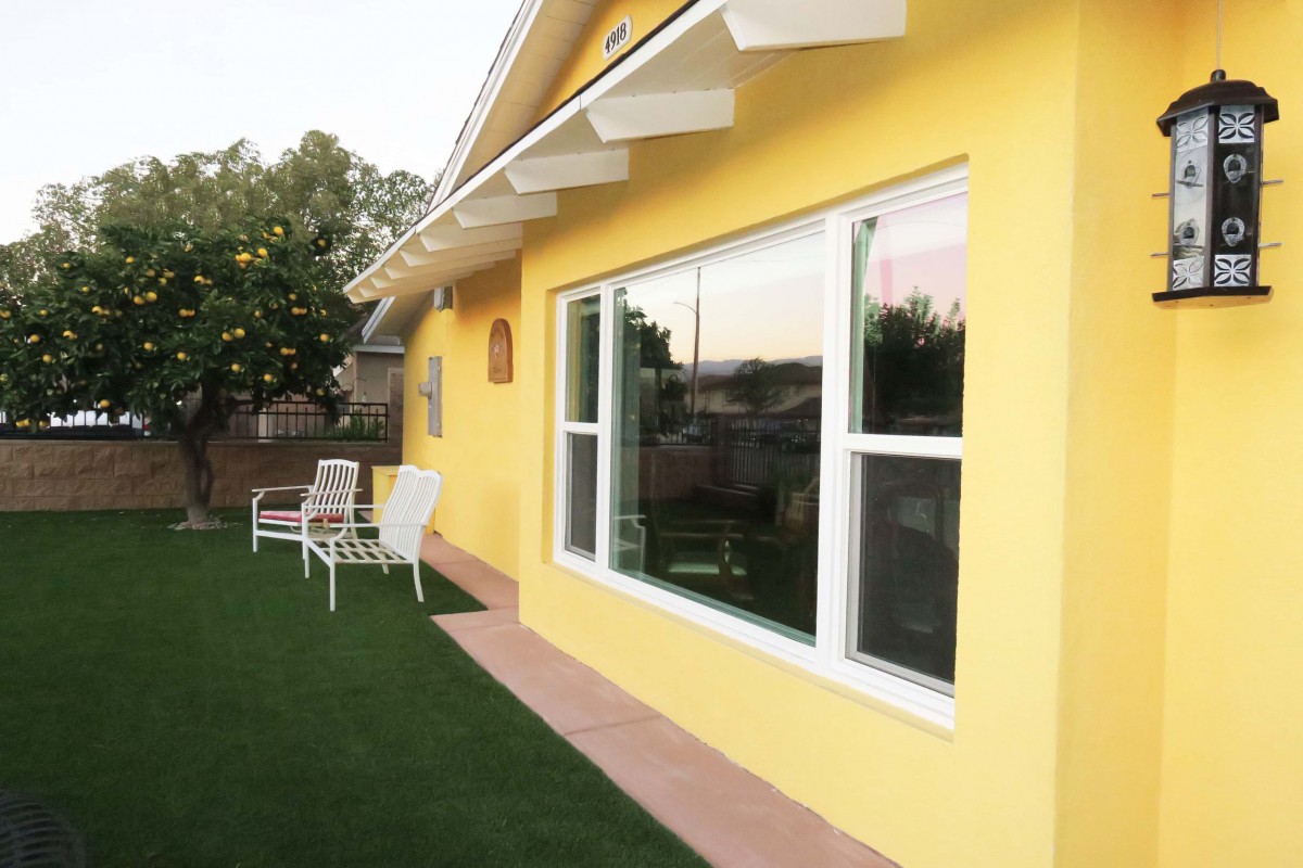 Sunny view of a house with a yellow exterior, featuring large windows and a grassy lawn.