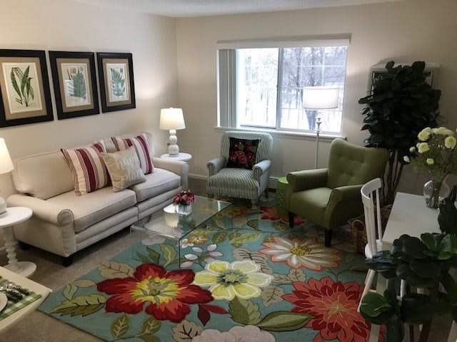 A cozy living room with colorful floral decor, featuring a sofa, armchairs, and bright lighting.