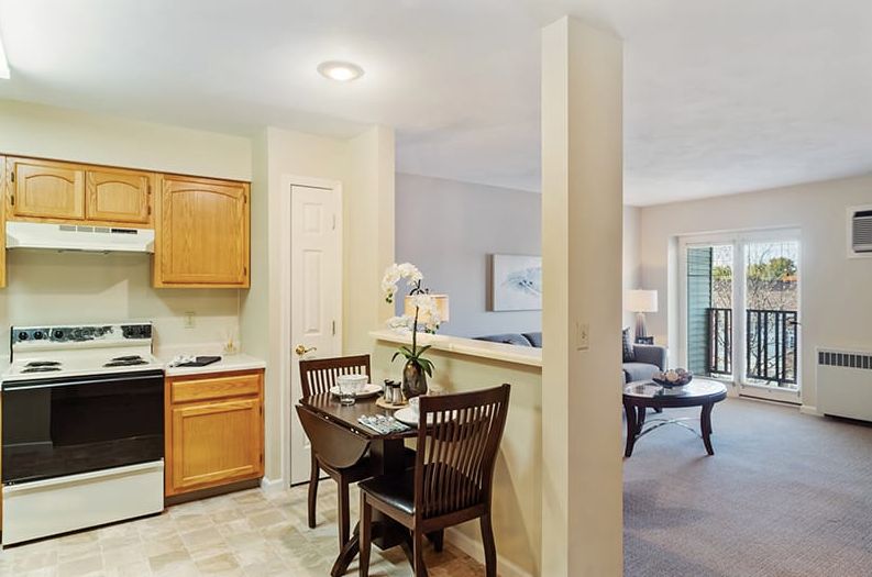 An open-concept apartment featuring a compact kitchen, a small dining area, and a glimpse of the living room.