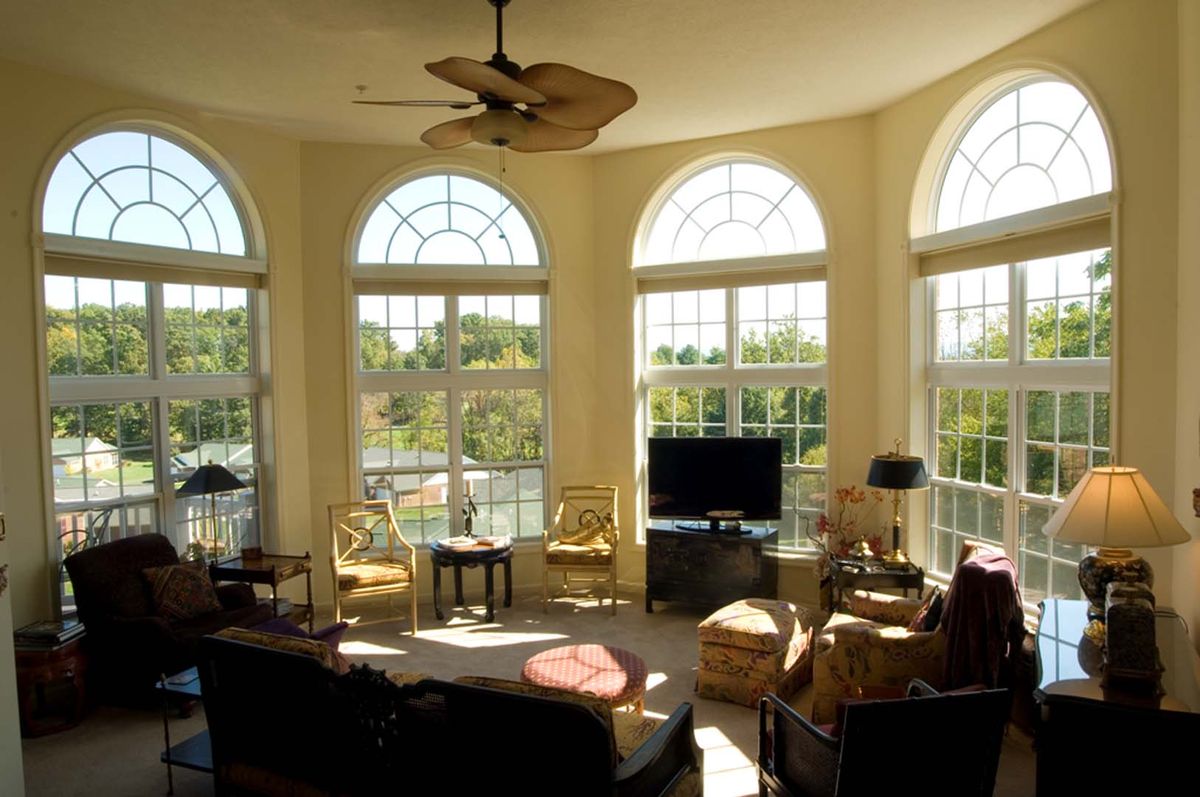 A sunlit living room with arched windows, elegant furniture, and a ceiling fan.