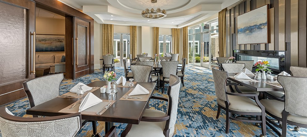 An elegant dining room with neatly arranged tables and chairs, featuring soft lighting and decorative elements.