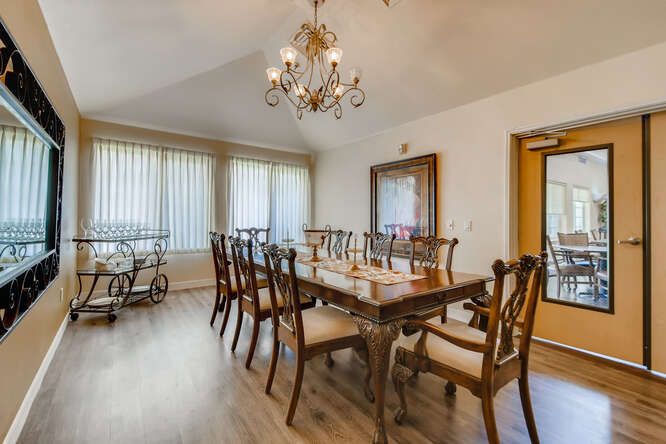 A spacious dining room with a large wooden table and chairs, illuminated by an elegant chandelier.