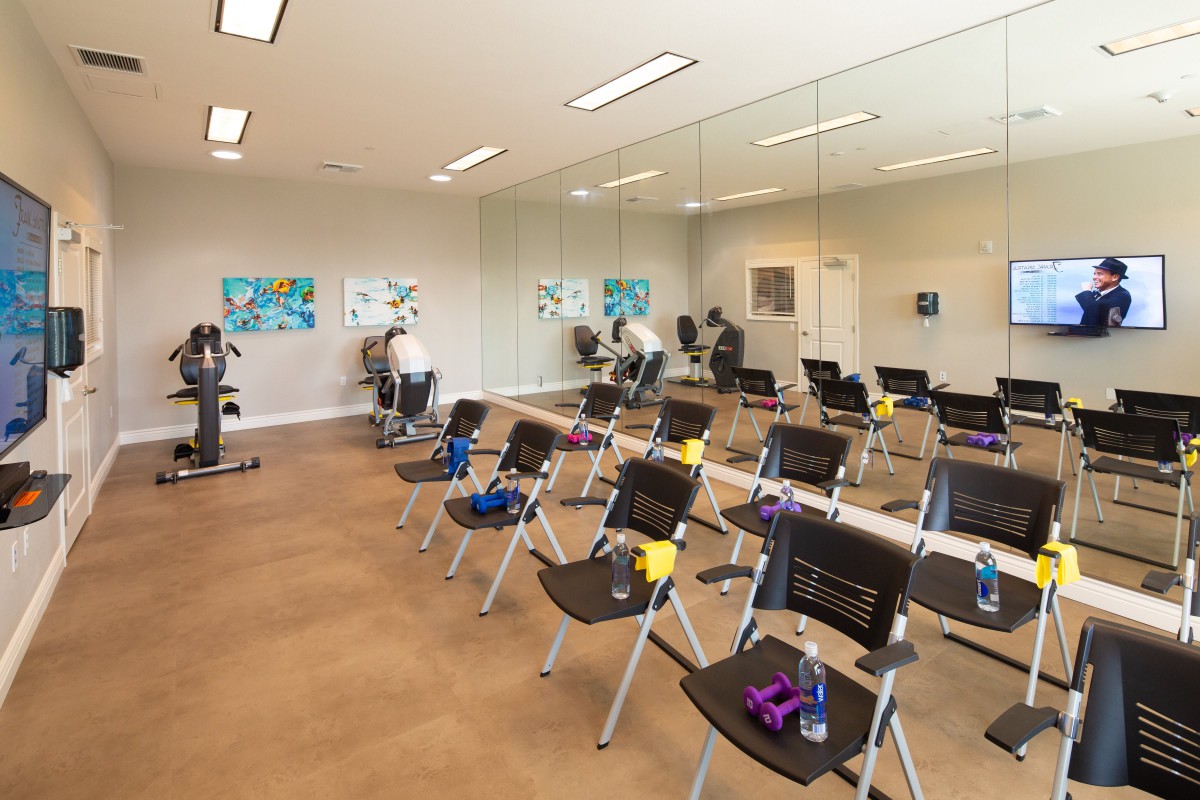 A spacious exercise room with chairs and fitness equipment lined up in front of large mirrors.