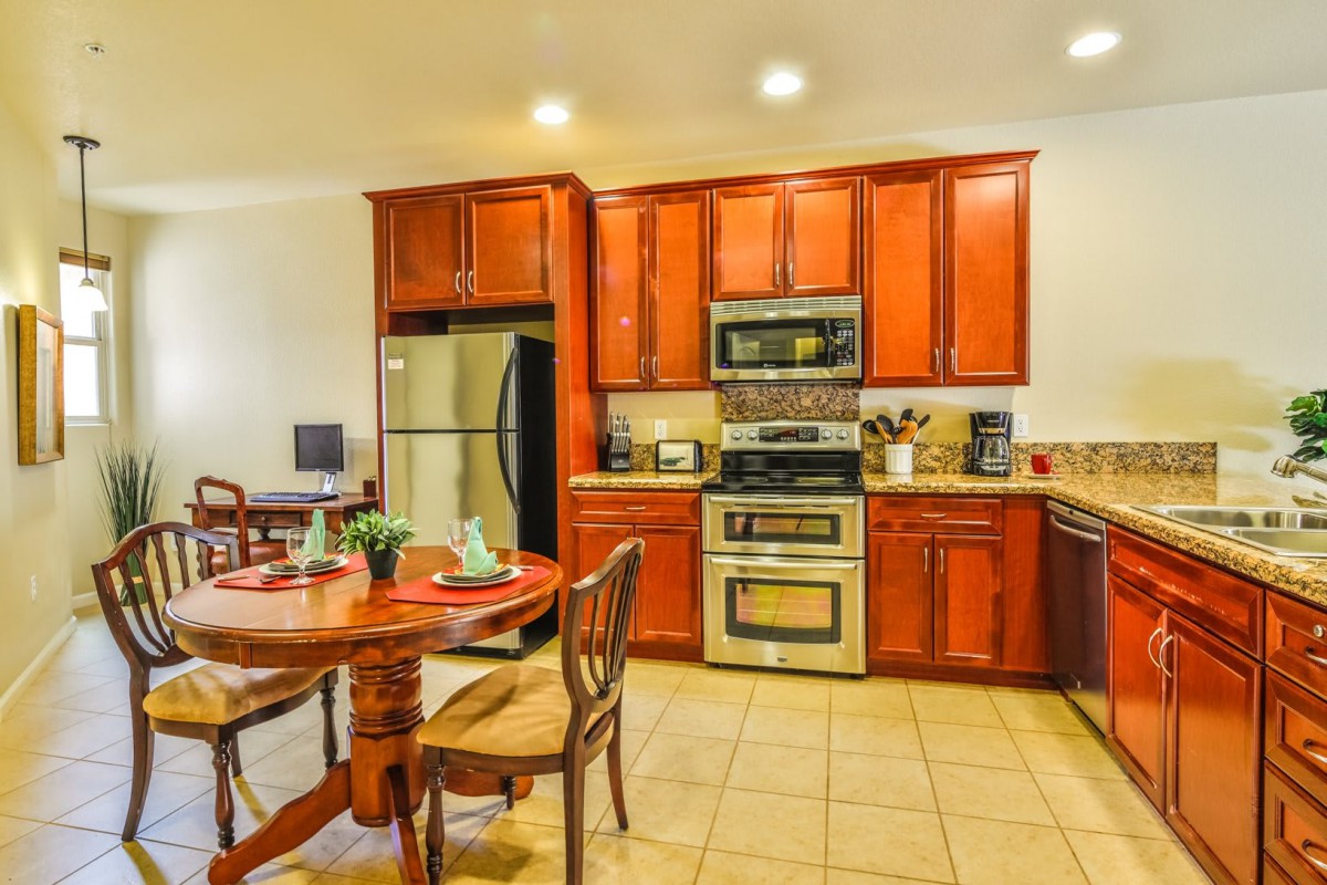 A modern kitchen with wooden cabinets and stainless steel appliances, adjacent to a dining area with a round table and chairs.