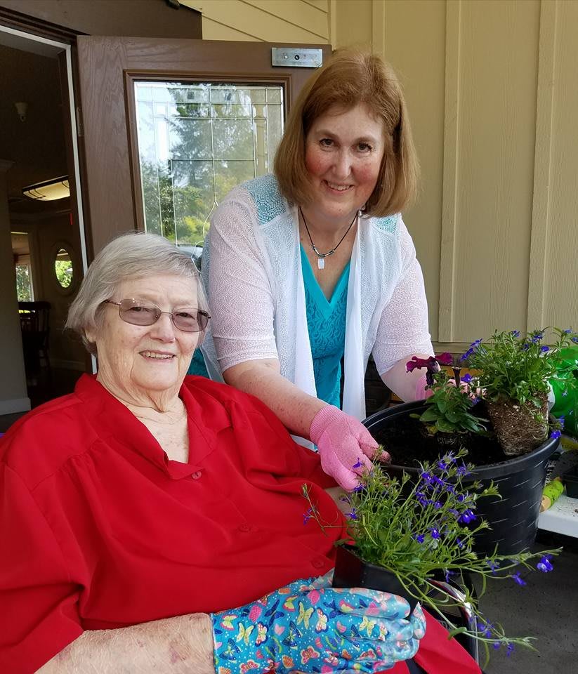 An elderly woman and a caregiver enjoying gardening together outdoors.