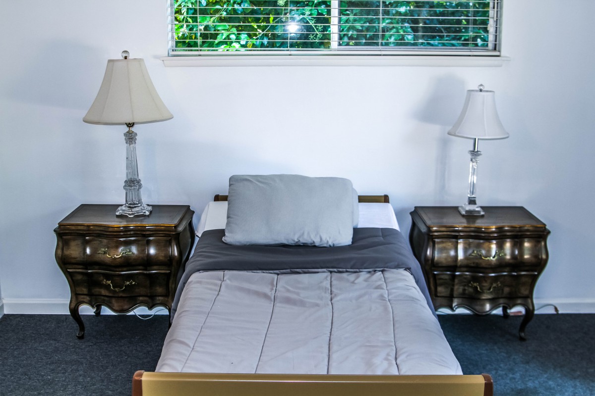 A neatly arranged bed between two nightstands with lamps, underneath a bright window.