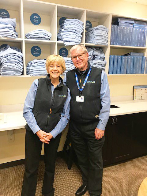 Two employees in uniform standing in a workplace with shelves full of folded clothes.