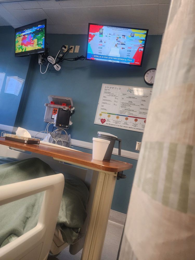 A view from a hospital bed showing medical equipment and a television on the wall.