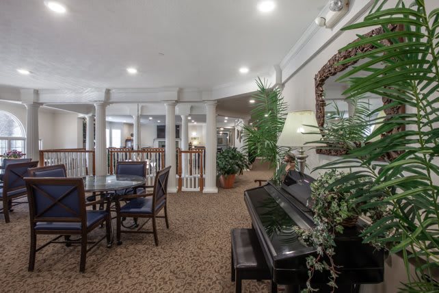 A cozy lobby area featuring a piano, tables, chairs, and decorative plants.