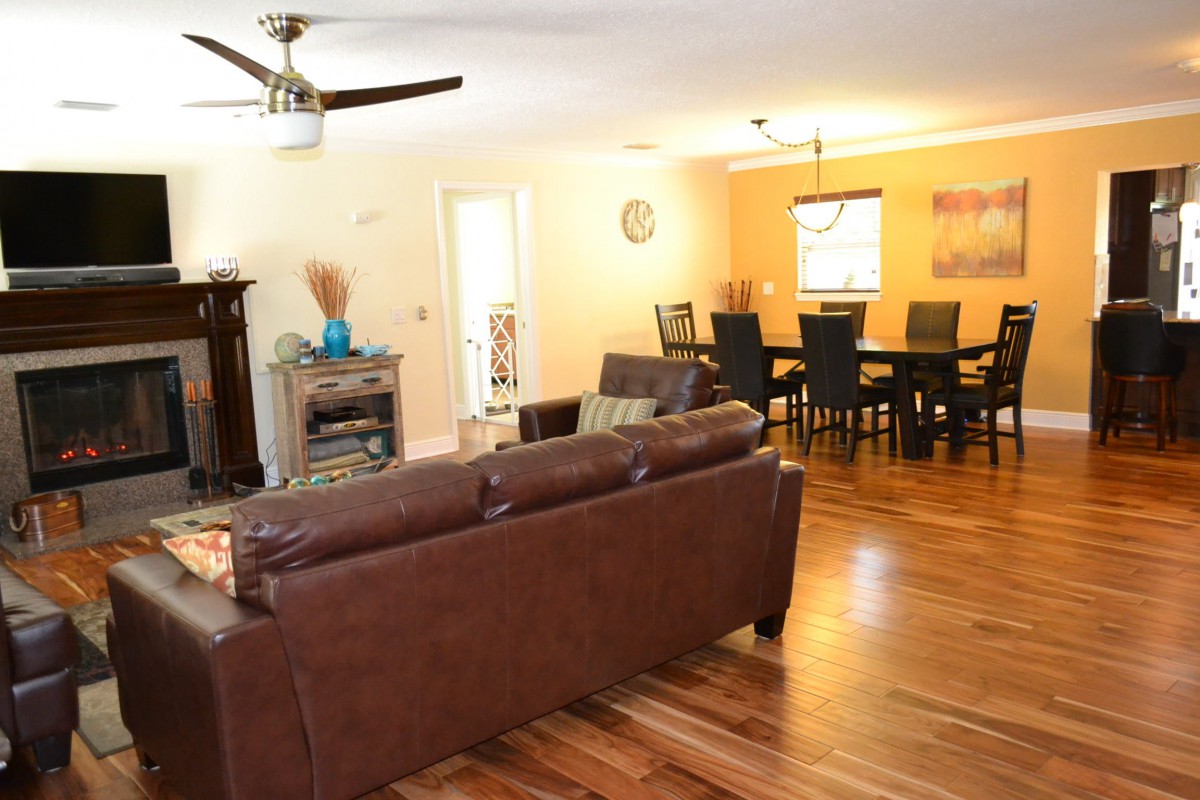 A spacious living and dining area featuring a brown leather sofa, elegant dining table, and warm wooden flooring.