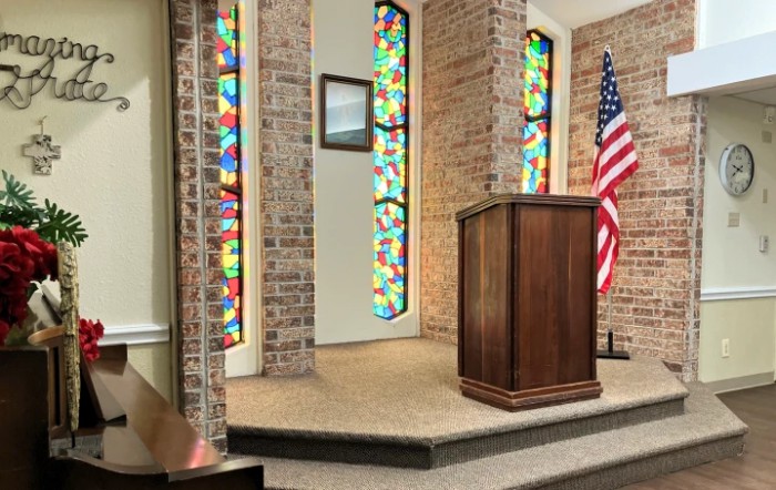 A church interior featuring a pulpit, colorful stained glass windows, and an American flag.