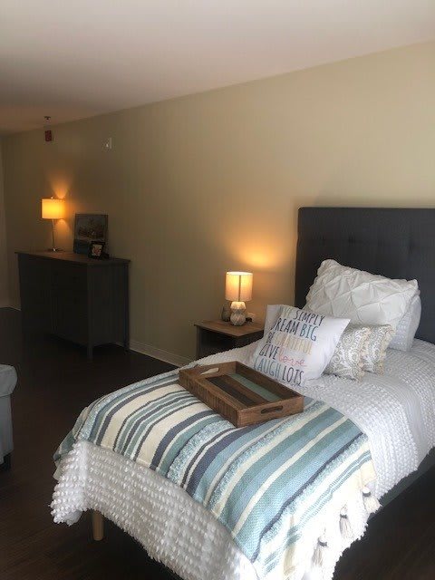 A cozy bedroom with a neatly made bed adorned with pillows and a decorative tray, softly lit by bedside lamps.