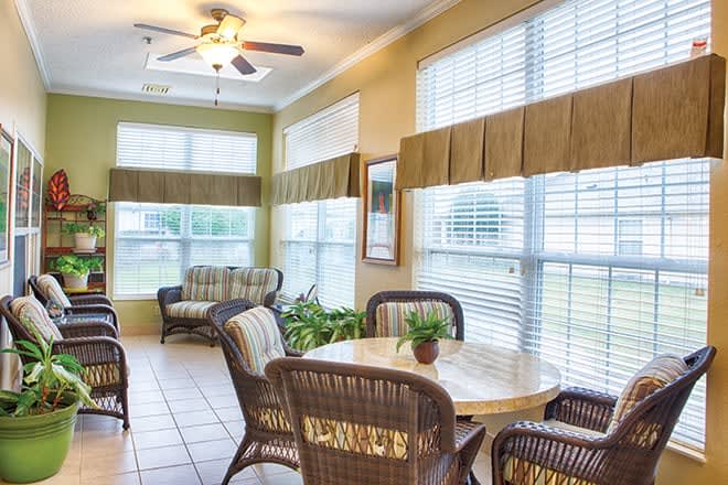 A cozy sunroom with large windows, wicker furniture, and a ceiling fan.