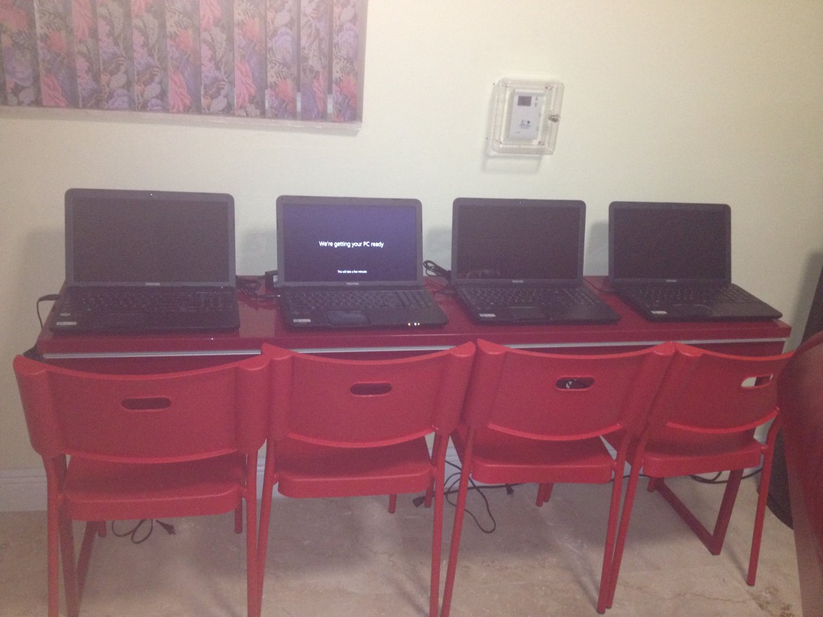 A row of laptops placed on desks with red chairs, likely in a classroom setting.