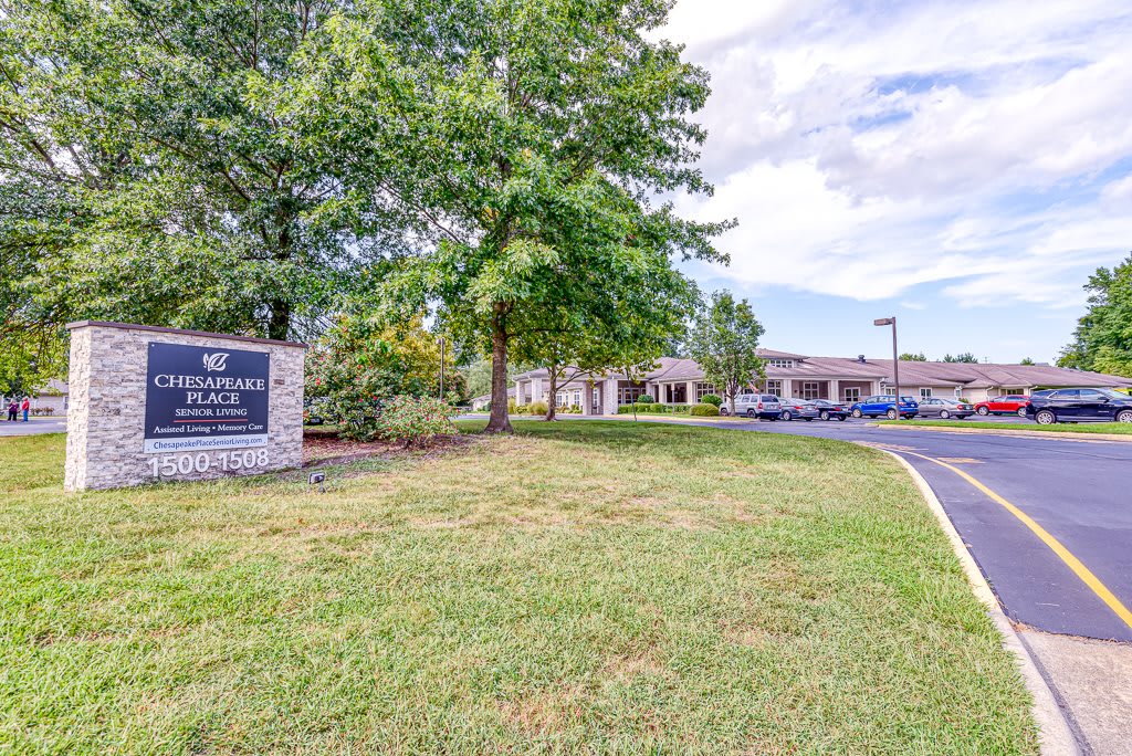 A view of a building with a sign, surrounded by trees and a lawn on a cloudy day.