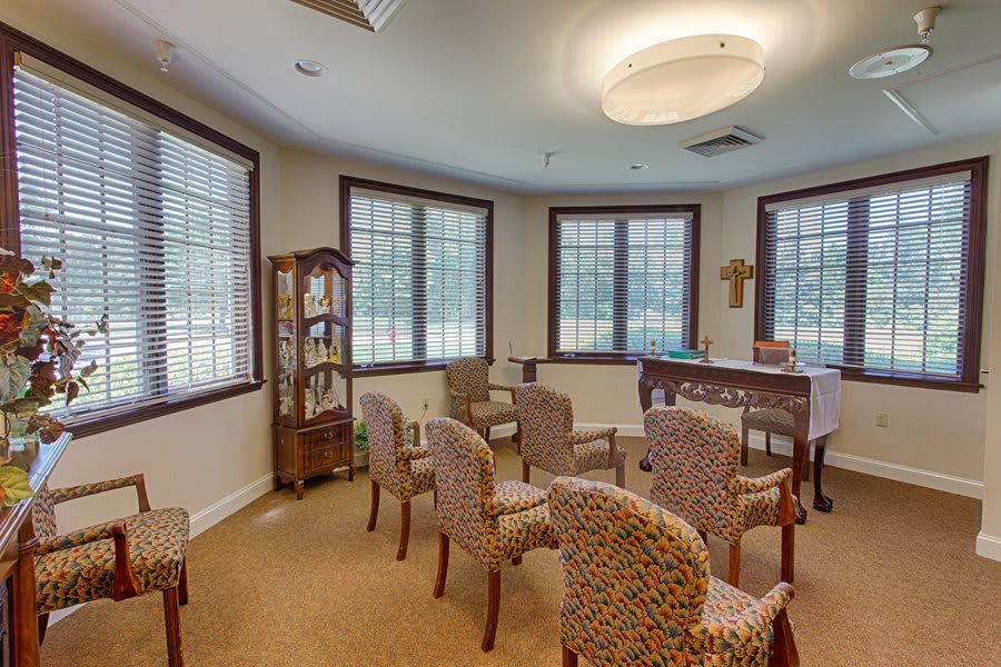 A small chapel room with chairs arranged in rows, large windows, and religious decor.