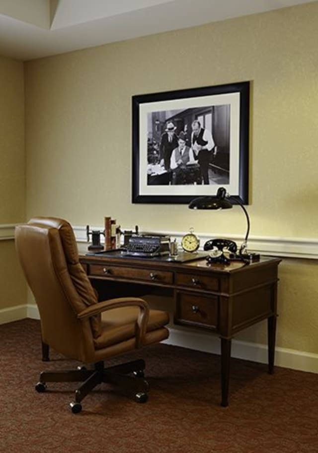 A vintage office setup featuring a typewriter on a wooden desk with a leather chair and framed photograph on the wall.