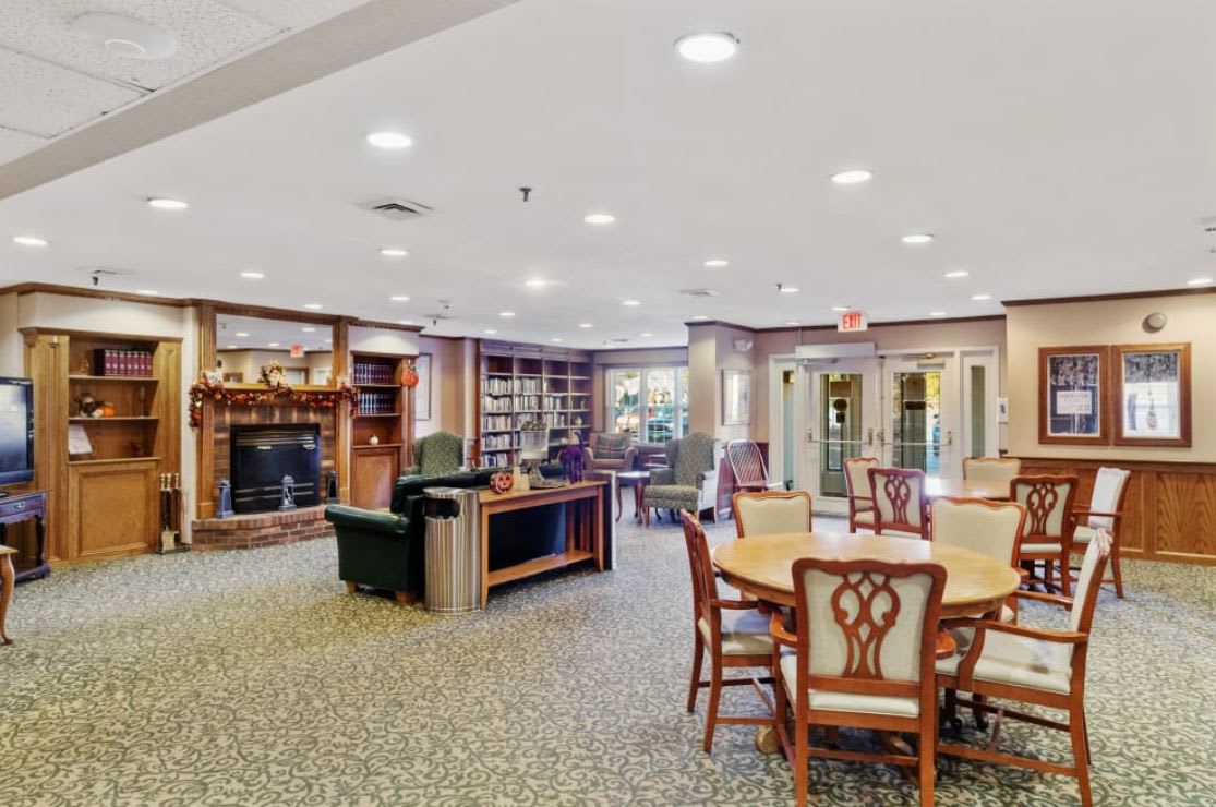 A cozy library interior featuring bookshelves, tables, and a fireplace.