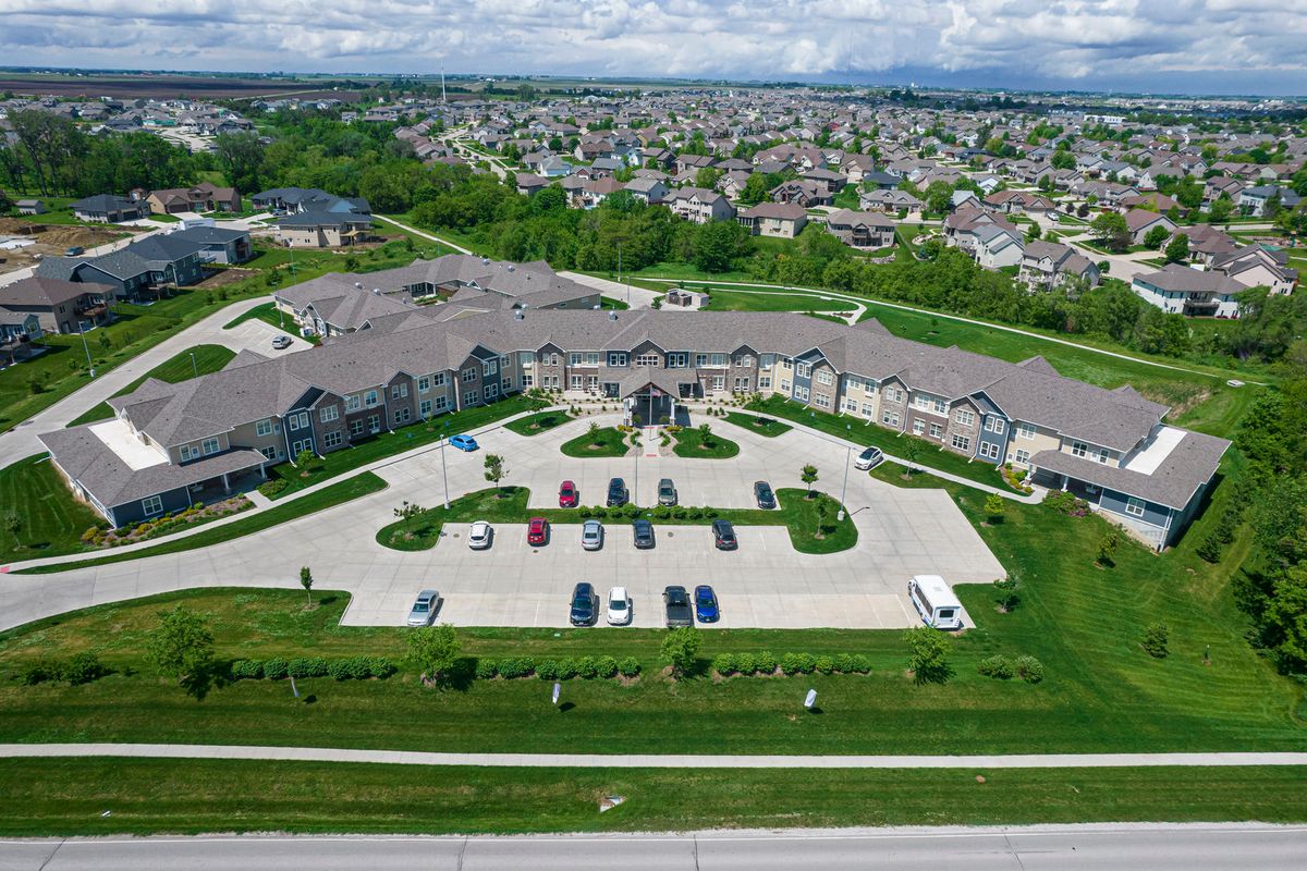 Aerial view of a large building with a parking lot surrounded by greenery and a residential area.
