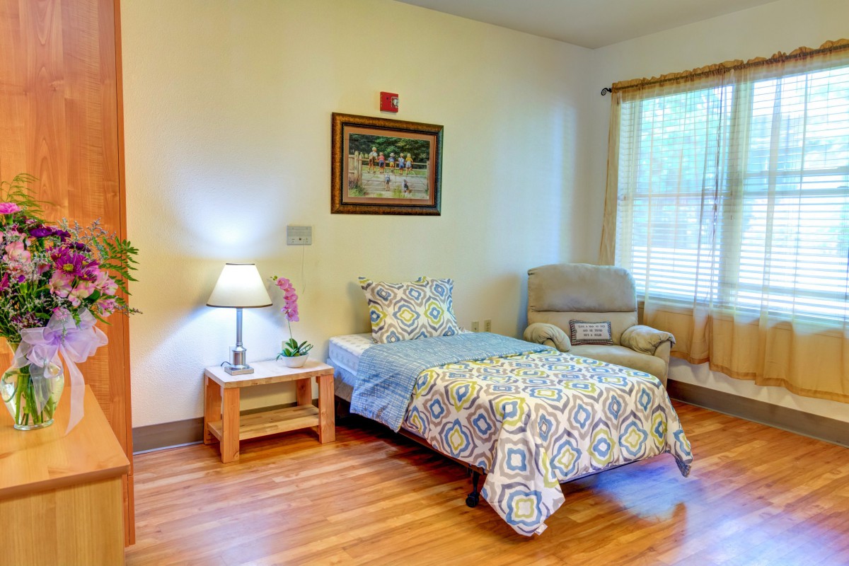 A cozy bedroom with a single bed, side table, and an armchair by the window.