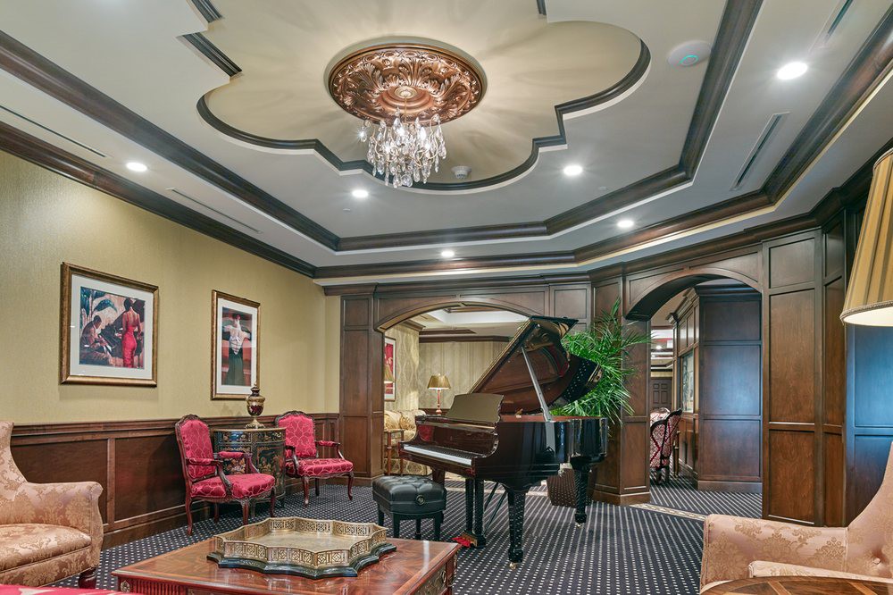 A luxurious living room with a grand piano and elegant furnishings under a decorative chandelier.