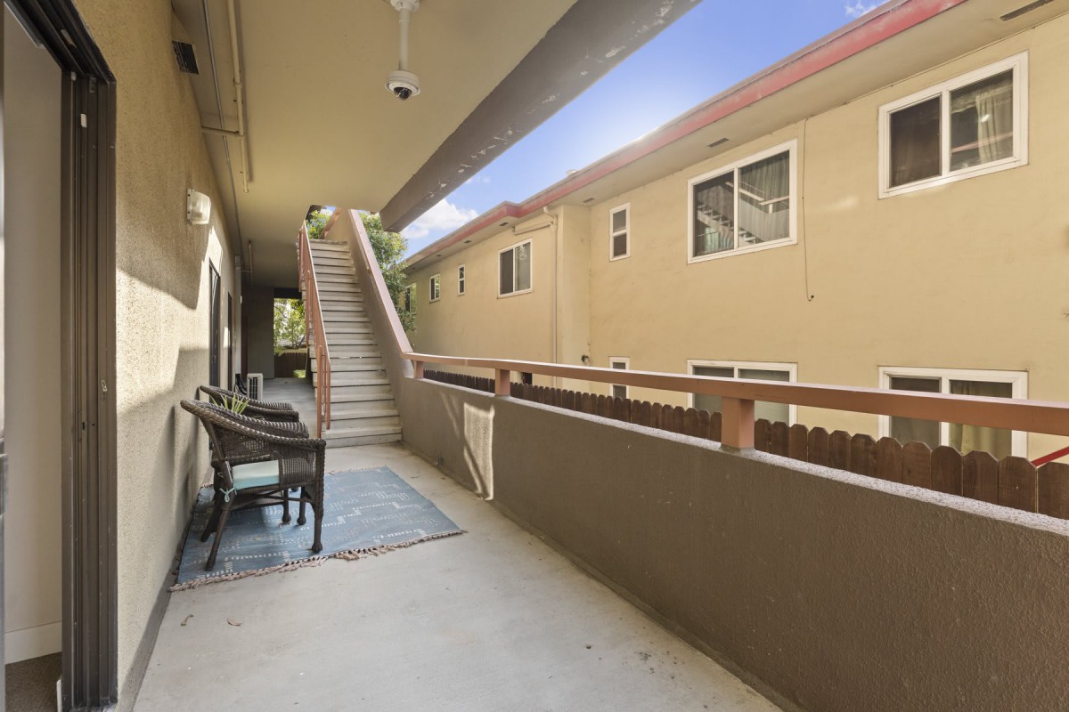 An outdoor corridor of an apartment building featuring stairs and railings under a clear sky.