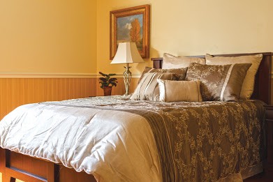 A cozy bedroom with a neatly made bed, decorative pillows, and a lamp beside a painting.