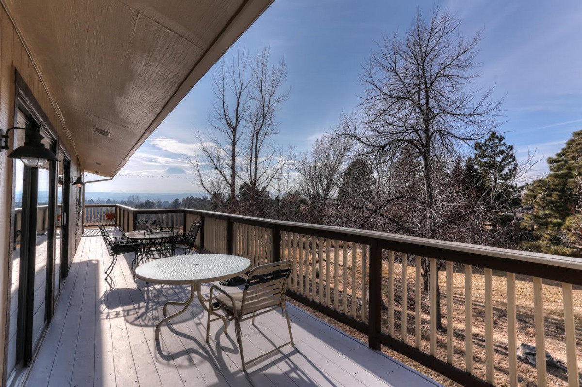 A spacious outdoor deck with tables and chairs overlooking a scenic view with trees and clear skies.