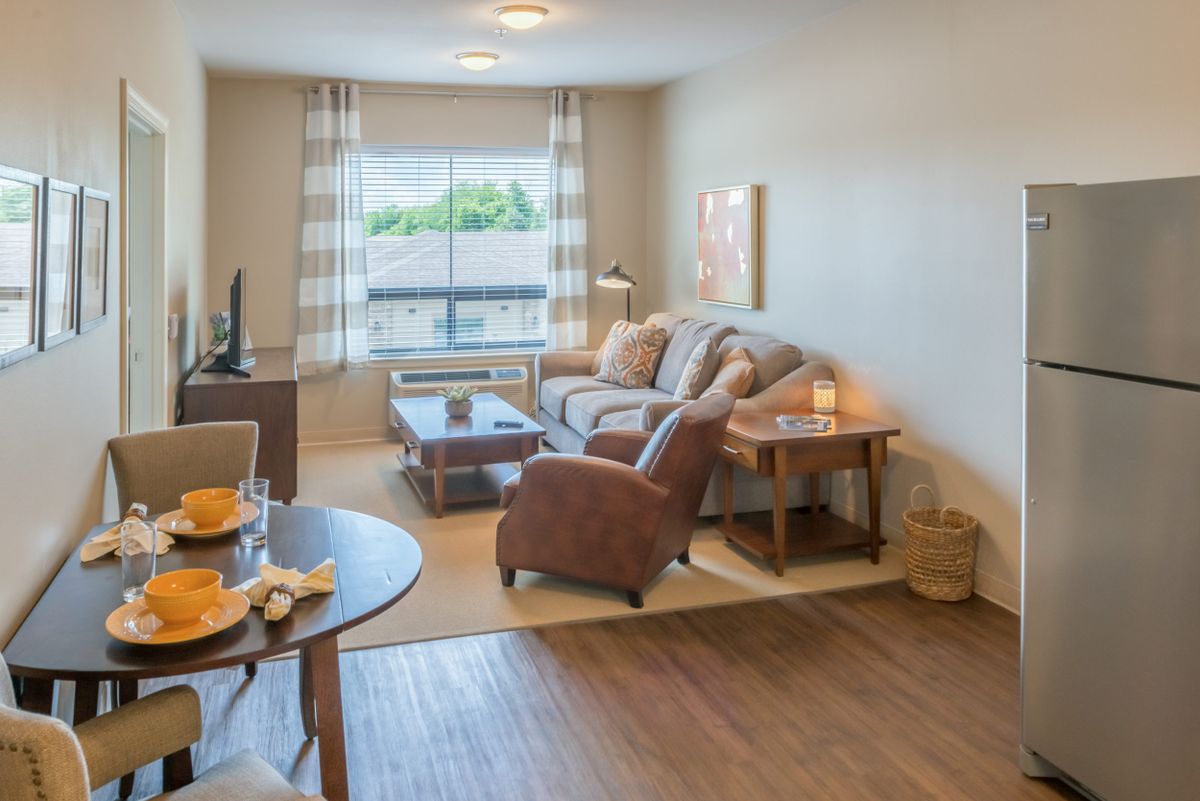 A cozy living room with a sofa, armchair, and coffee table, complemented by a dining area and large window.