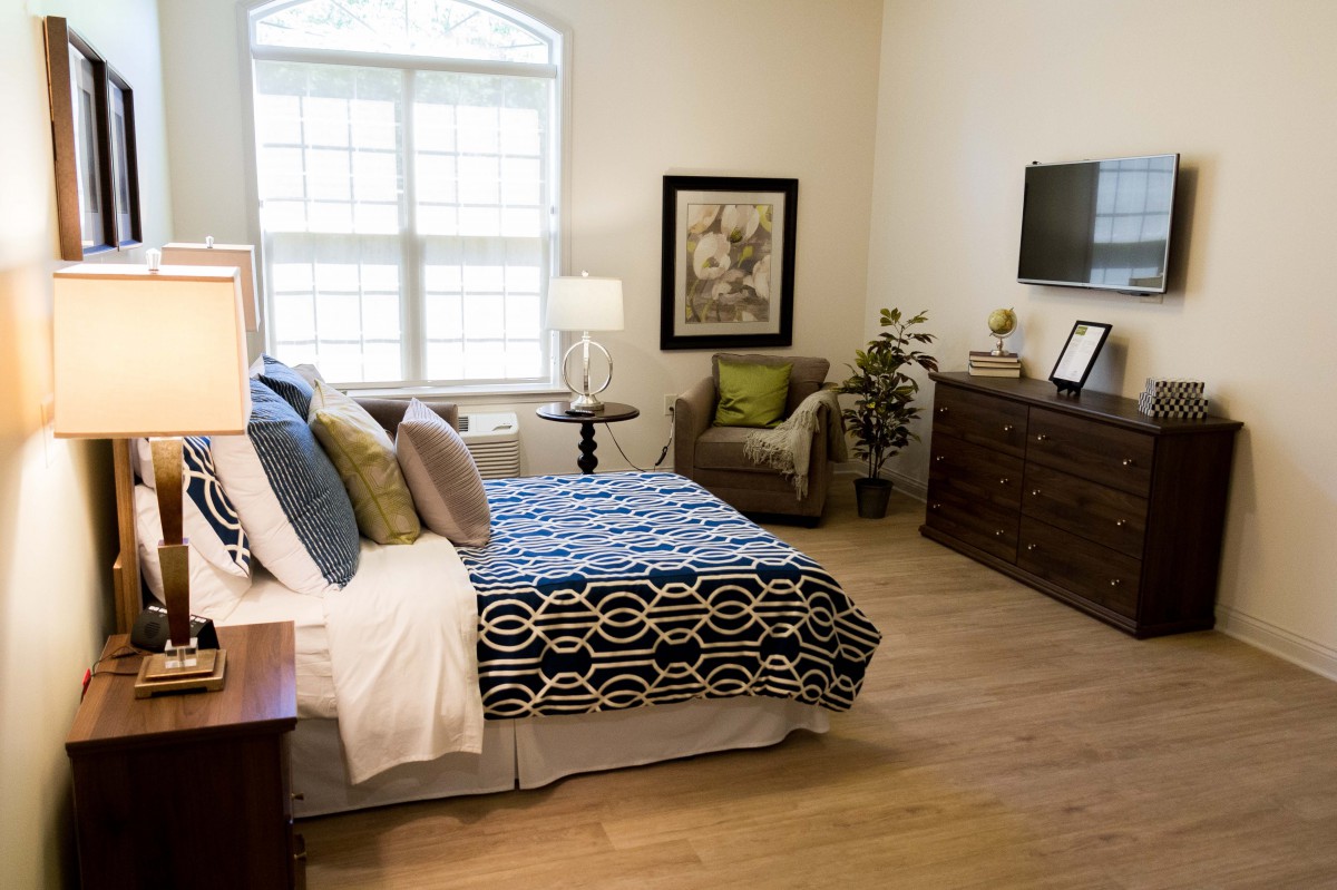 A modern and cozy bedroom featuring a bed with patterned bedding, a TV mounted on the wall, and elegant furnishings.