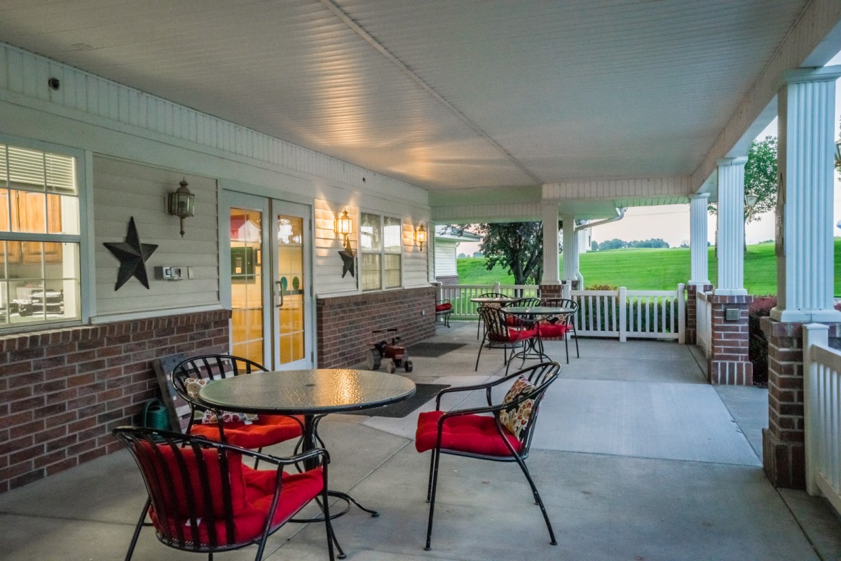 A cozy covered patio with tables and chairs, illuminated by warm lighting.