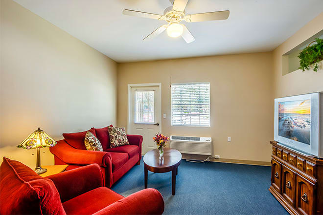 A cozy living room with a red couch and armchair, featuring a coffee table and a ceiling fan overhead.