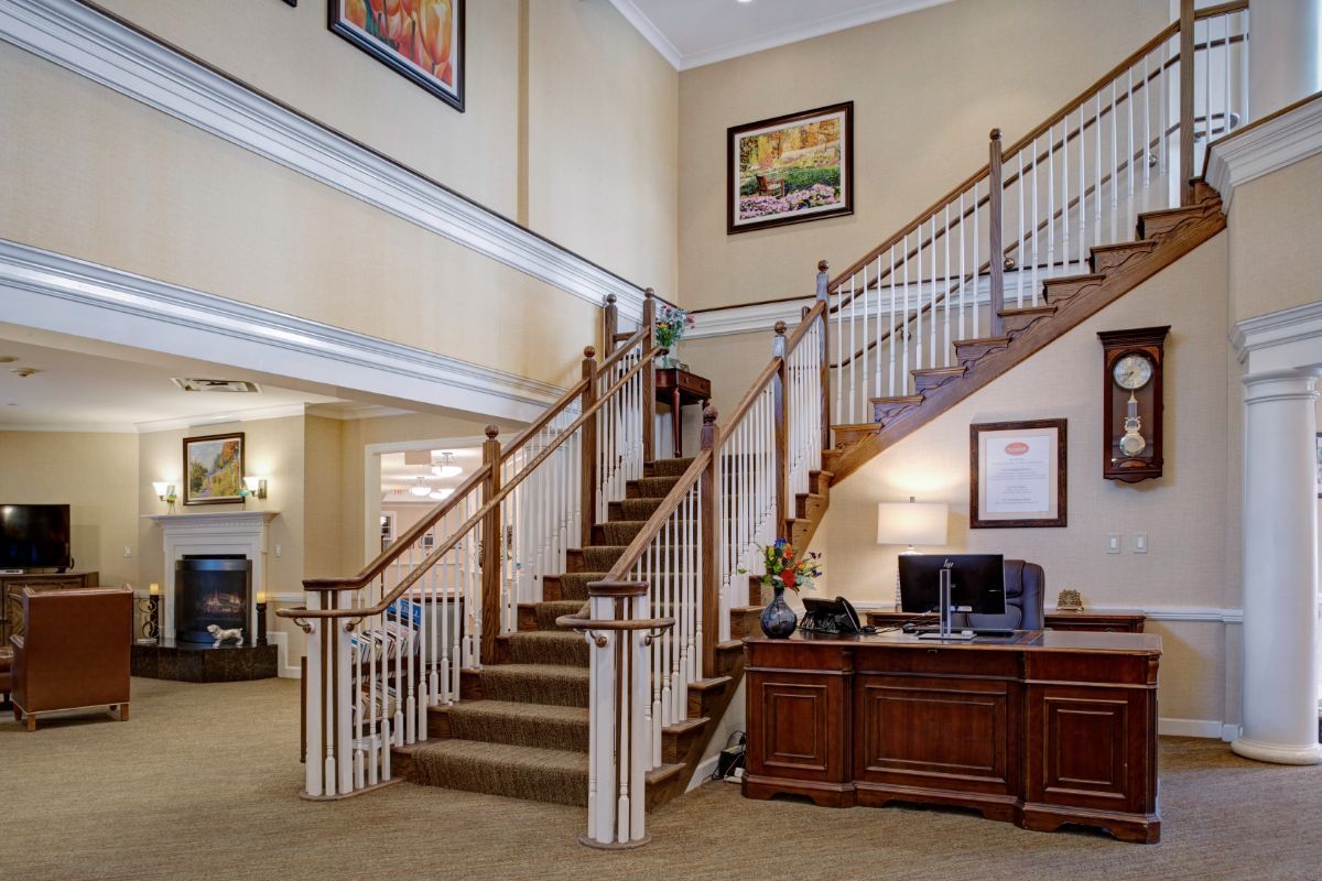 A spacious interior with a central staircase and a reception desk, adorned with framed artwork on the walls.