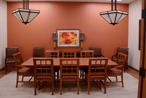 A cozy dining room featuring a large wooden table surrounded by chairs, set against an orange wall with decorative lighting and artwork.