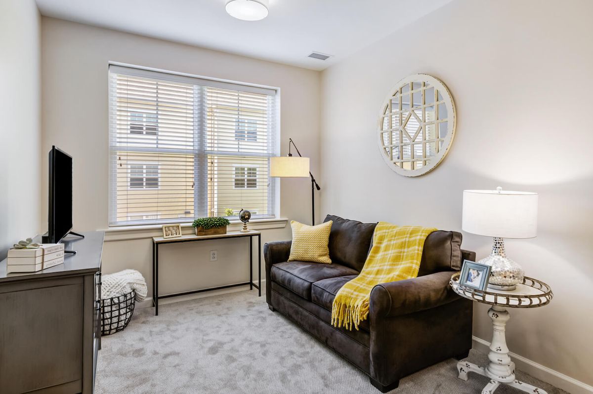 A cozy living room with a sofa, decorative pillows, and a large window, featuring a mirror and warm lighting.