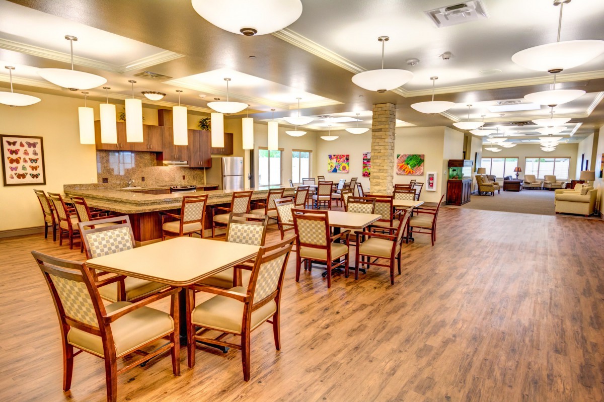 A spacious dining area with neatly arranged tables and chairs, featuring warm lighting and wooden flooring.